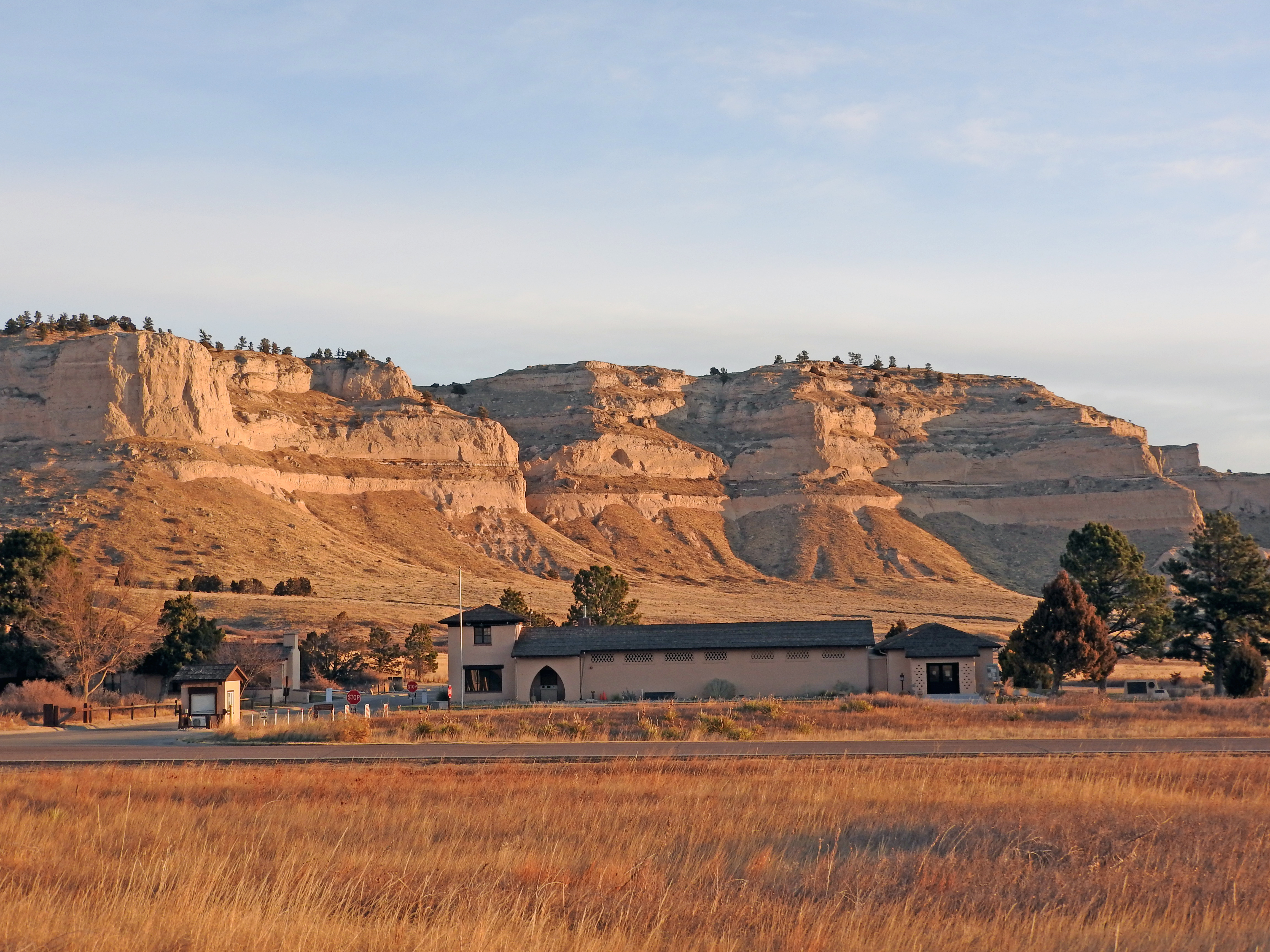 A building is bathed in red morning light with a sandstone bluff in the background.