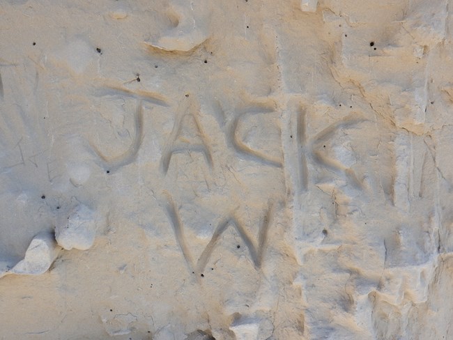 Graffiti that reads "Jack W" is carved into a sandstone rockface.