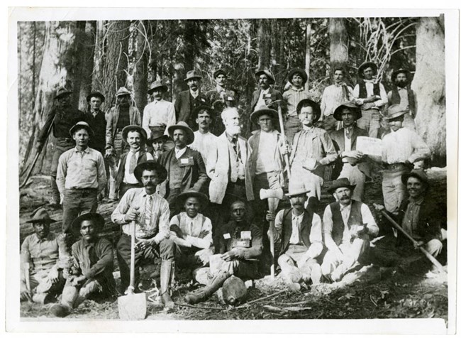 Photograph of a group of men, the Sequoia National Park road crew, with Charles Young in middle, posing in front of a forest, 1903
