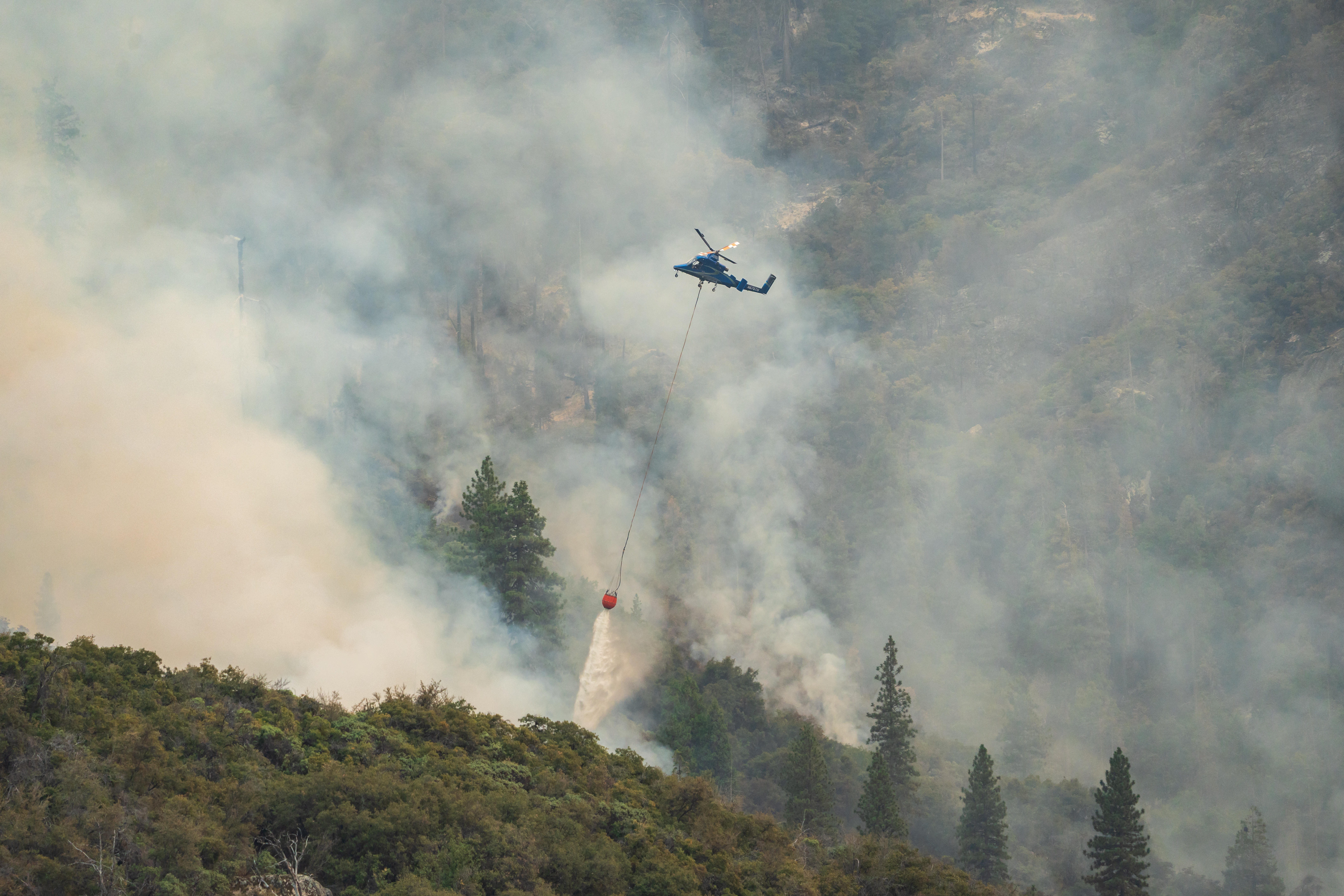 A helicopter releases water onto a smoke-filled hillside during the Coffee Pot Fire.