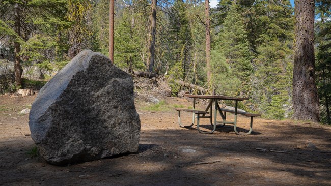 A picnic table next to a large granite rock.