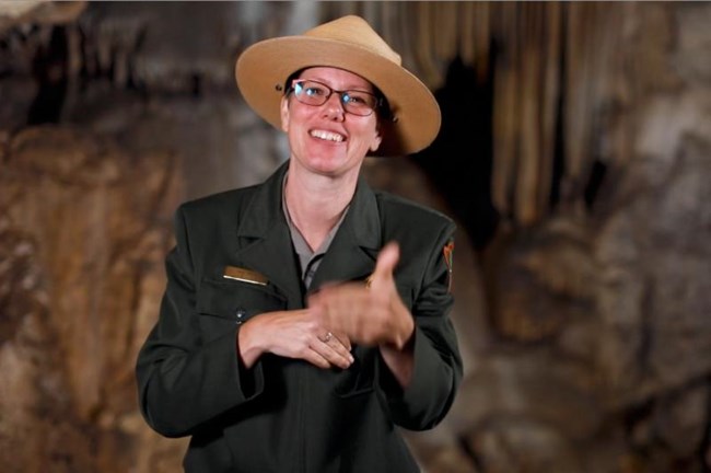 A female National Park Service ranger in uniform signs to a person not pictured. Photo by Brian Peterson