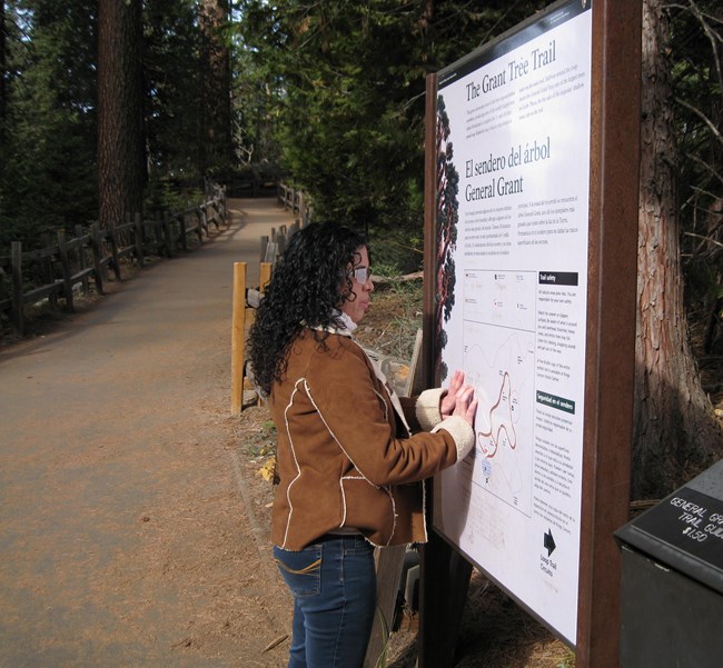 A woman reads Braille text on an orientation sign at the Grant Tree Trail.
