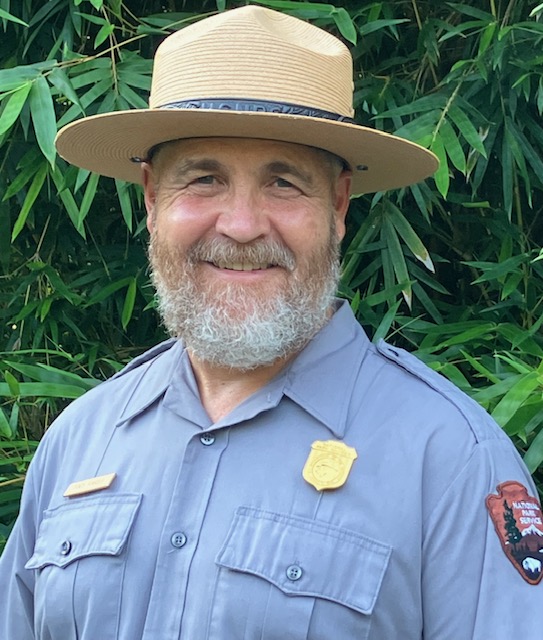 A man with a beard, wearing an NPS uniform and flat hat, smiles