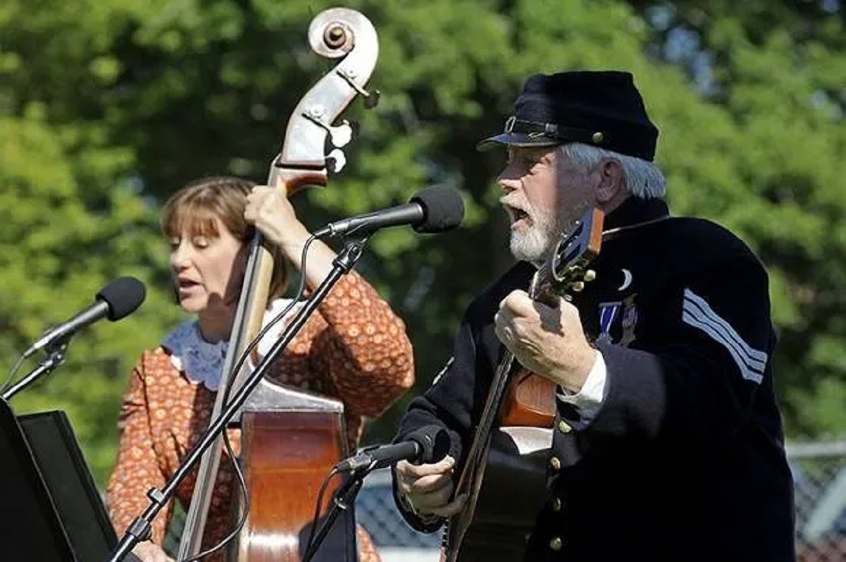 A man and woman in period clothing playing instruments and singinf