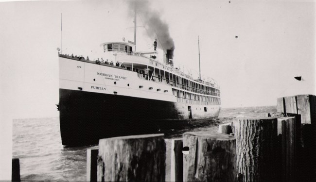 Black and white picture of a large steamboat, "Puritan", arriving at a dock with passengers.
