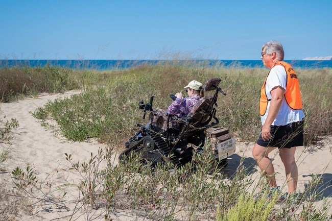 A person in an off-road wheelchair rides on the beach