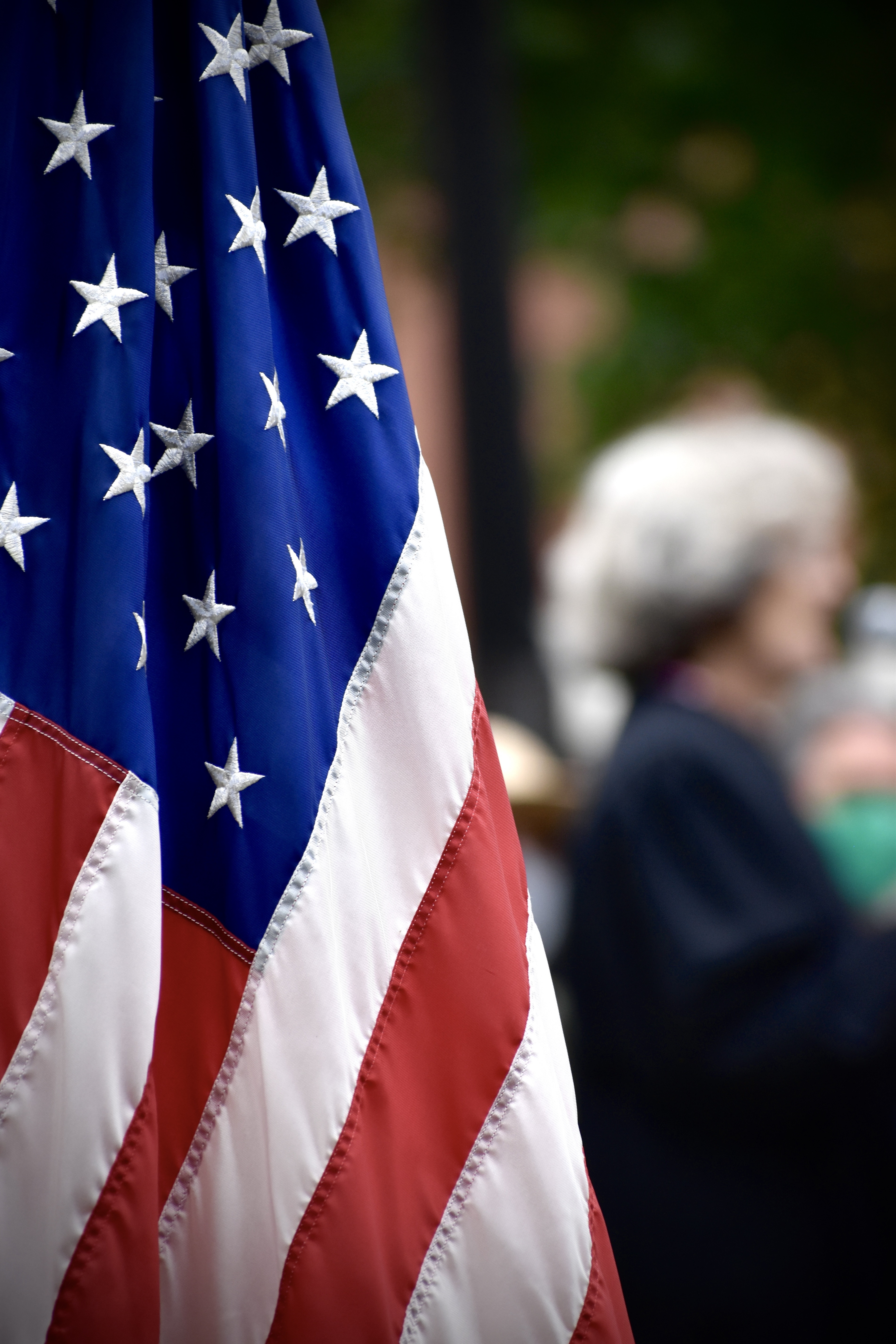 A United States of American flag in the forefront with a person in the background.