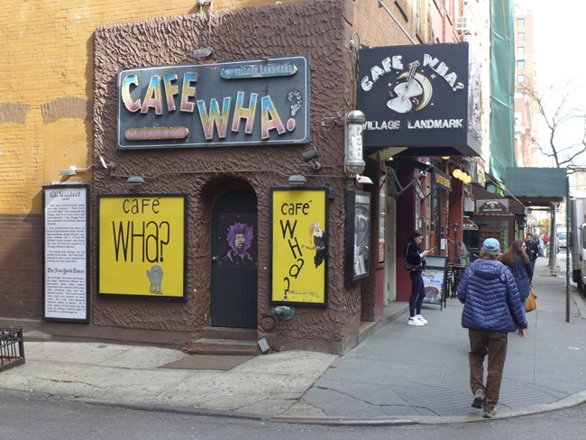 Outside the Cafe Wha? calling itself a Village landmark. A painting of Jimi Hendrix is on one door.