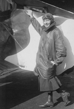 A young woman stand in front of a plane with her hand touching it