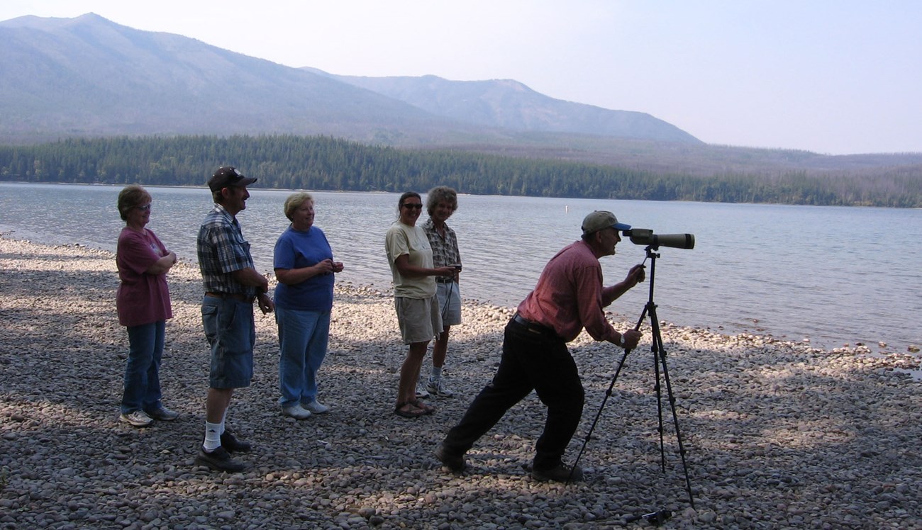 Six people gather on a rocky beach with a spotting scope.