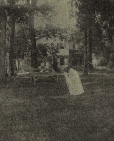 A fuzzy photo of a young girl in a white cress, played croquet in a yard under tall, straight trees.