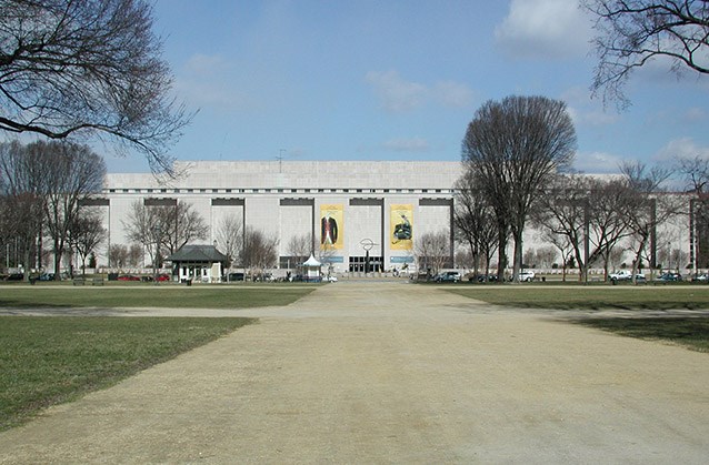 View of the National Museum of American History following 13th Street, with elms arising in the foreground of the building on either side of the broad walkway leading to its doors.