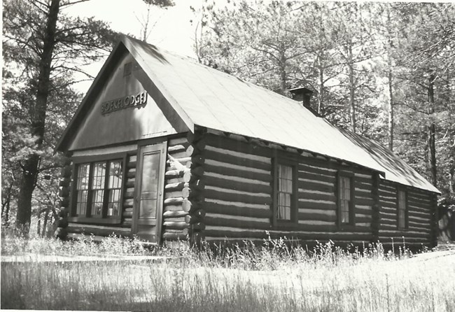 One-story cabin with saddle notched logs, a gable roof, and the word "Boekelodge" over the front door and windows.