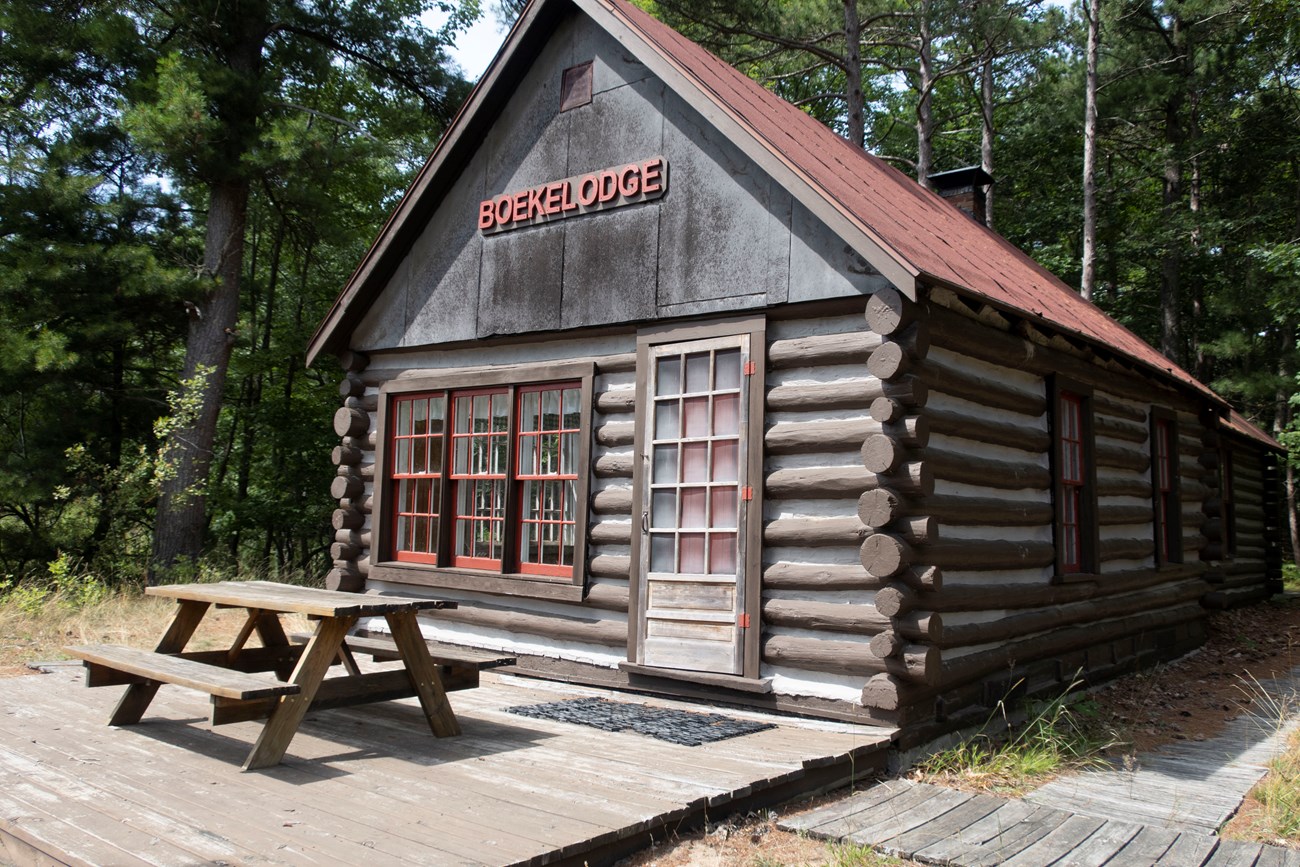 A log cabin with a pitched roof and the word "Boekelodge" on the front, with a picnic table on a platform in front