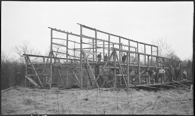 A black and white photo of crew members working on the wooden frame of a structure.