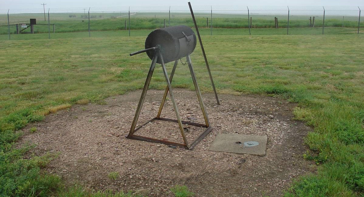 The code burner is a cylindrical device on a triangular base, surrounded by open lawn.