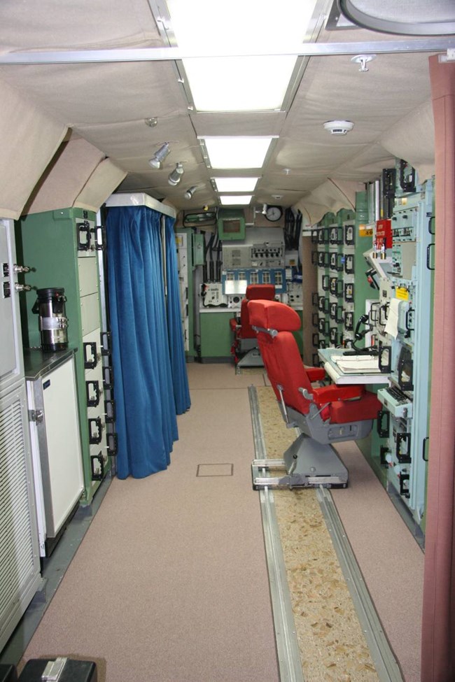 Long, narrow launch control center with control panels and command chairs