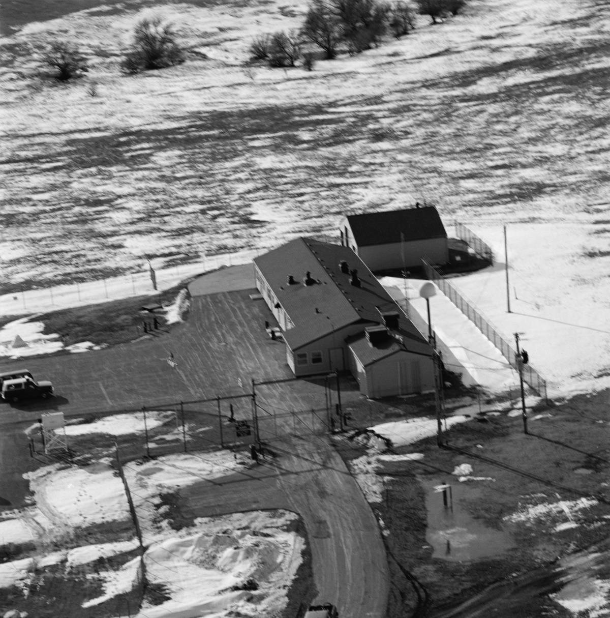 Aerial view of Delta-01 with road leading to building cluster, surrounded by open snowy fields.