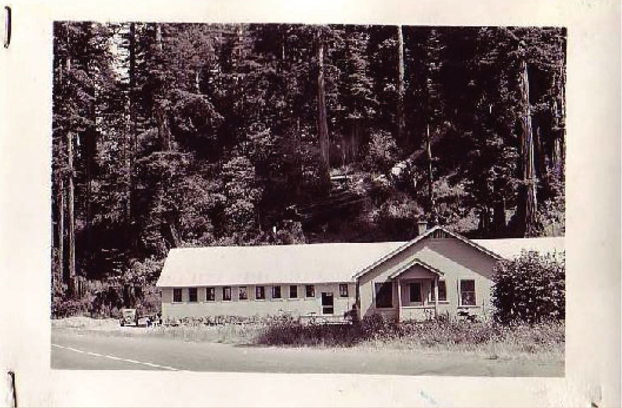 A long, one-story hatchery building between a road and a hillside covered by trees.