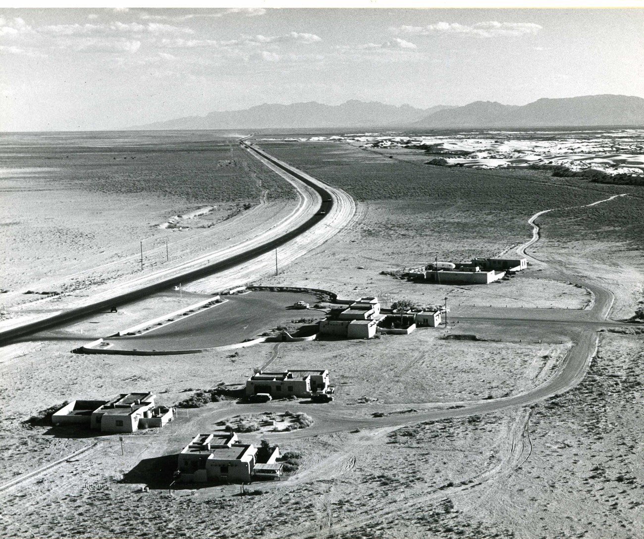 This historic photo provides an aerial view of White Sands' housing, visitor center, and maintenance complex, a cluster of buildings near a curving road.