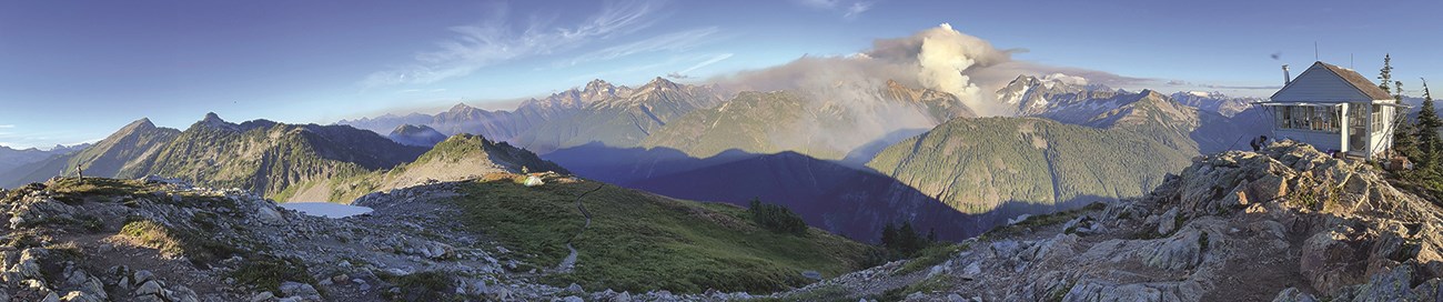 Panoramic view of smoke rising from snowy mountains with a fire lookout in the foreground.