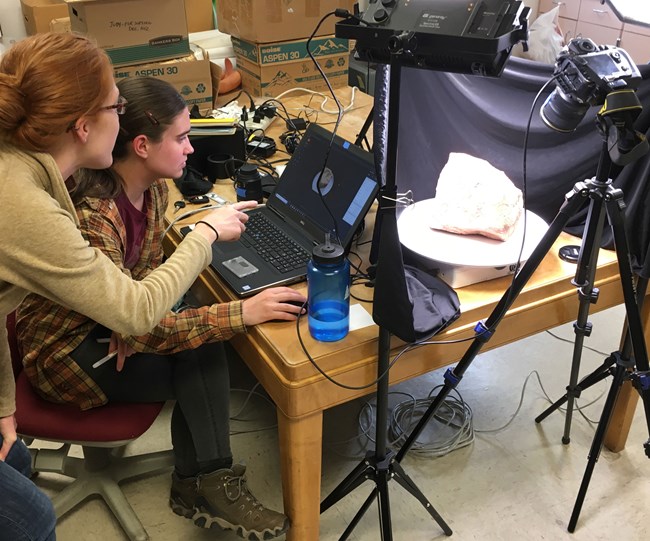 grca-fossil-modeling-crop two people work at a computer with camera and lights set on rock sample
