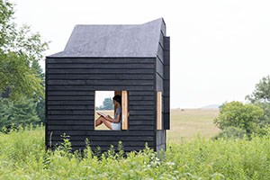 A person sits and writes in a mobile studio in a meadow.