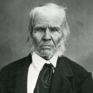 Historic black and white photo of elderly man with white hair in black jacket.