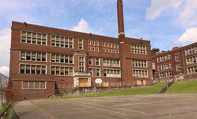 3-story red brick school building with basketball court in front.