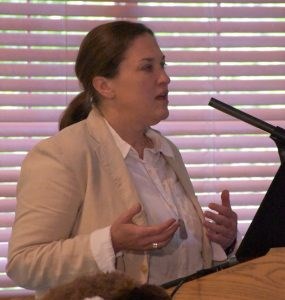 White female with hair pulled back in a ponytail wearing a cream-colored jacket over a white shirt.