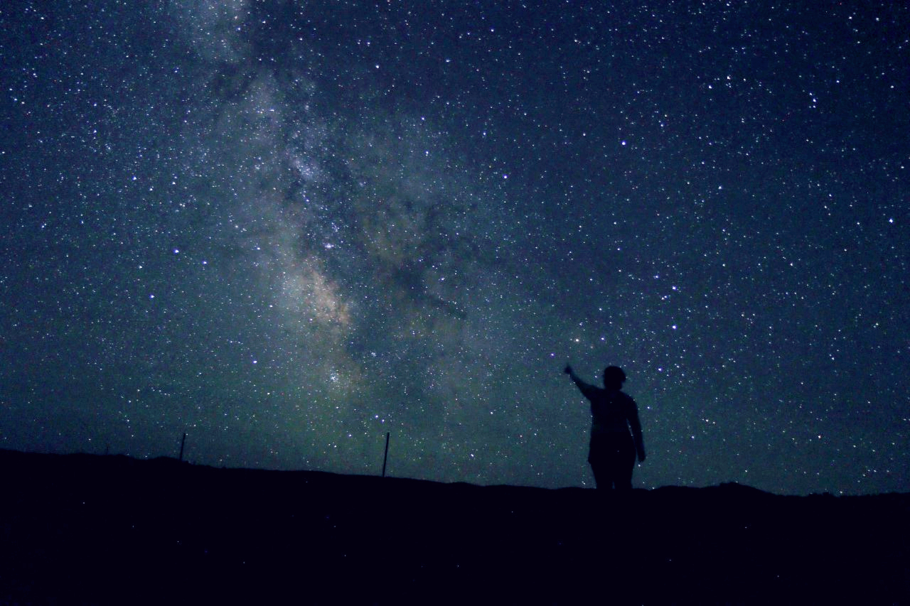 Silhouette of a person standing against the night sky filled with stars
