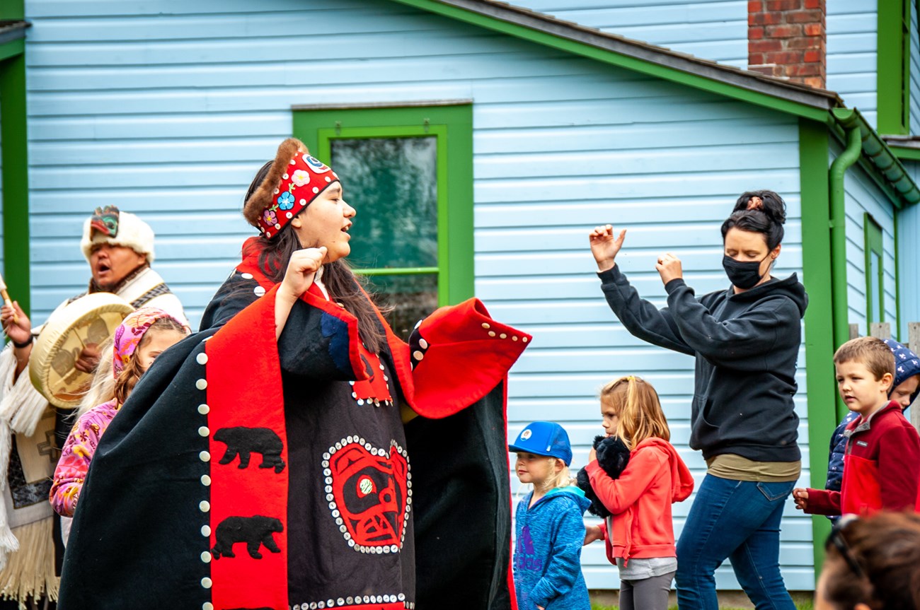 Jilkaat Kwaan Heritage Dancers with a group of young children and a masked woman, dancing