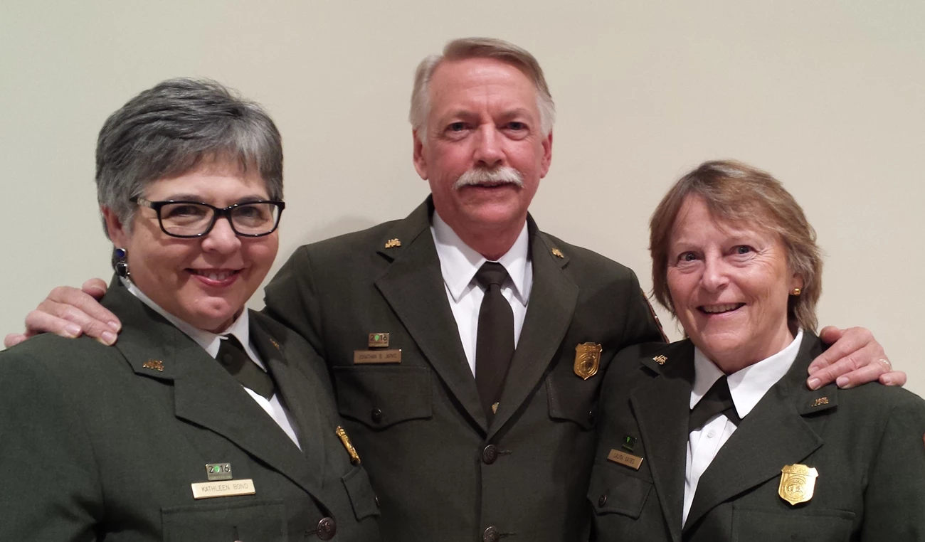 Kathleen Bond in NPS uniform Three people, Kathleen Bond, Jon Jarvis, and Laura Gates, pose in the green jacket and pins of NPS uniform,