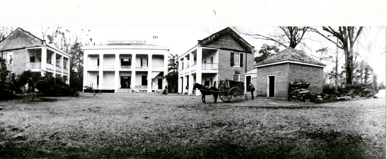 Melrose Backyard in 1905 Three large, two-story structures with columns and porches are arranged to form a courtyard. A horse and carriage stand in the yard.