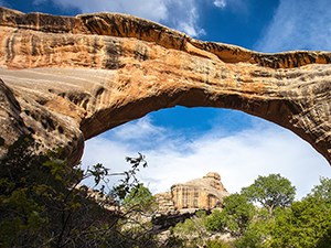 Unlocking Earth's Secrets, Layer by Layer Photo of a colorful, natural stone bridge, framing a landscape with colorful rocks and trees.