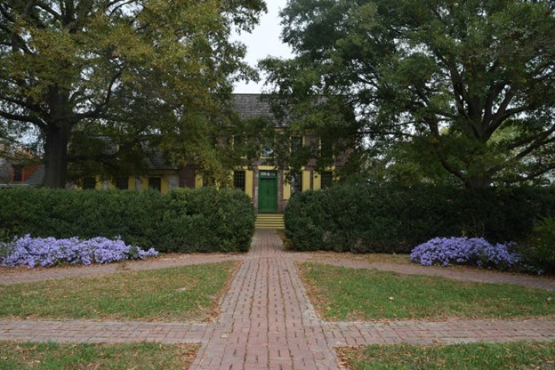 Red brick walkway leads up to the John Dickinson Plantation, a large yellow house surrounded by mature trees.