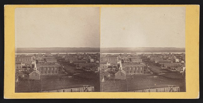 Farnam Street from hill west of city, c1868. Two story brick buildings, smaller frame buildings, dirt roads. Missouri River clearly visible and opposite bank empty.