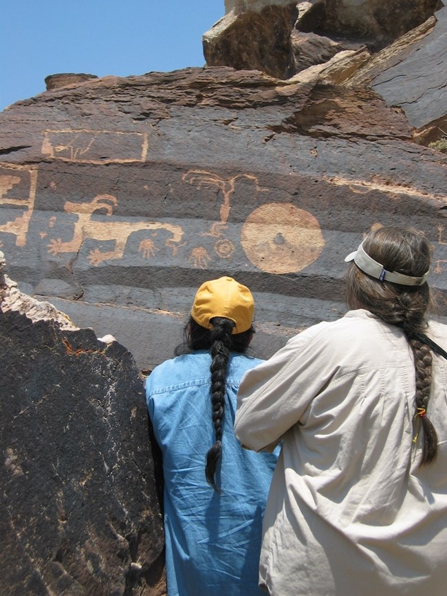 People view petroglyphs carved into rock.