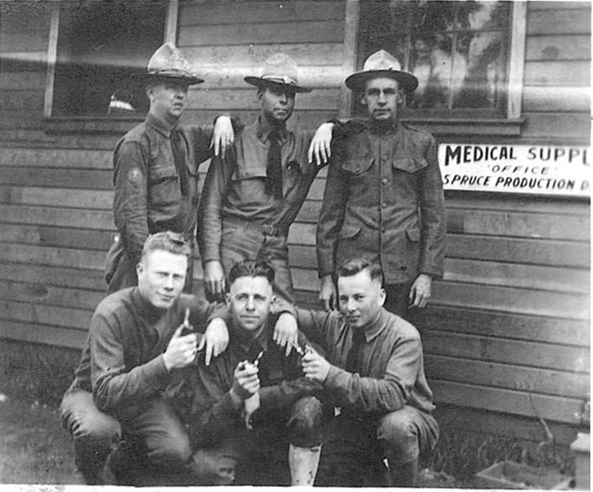 Black and white photo of six men posing in front of a building with a sign that reads "Medical Supply Office, Spruce Production Division."