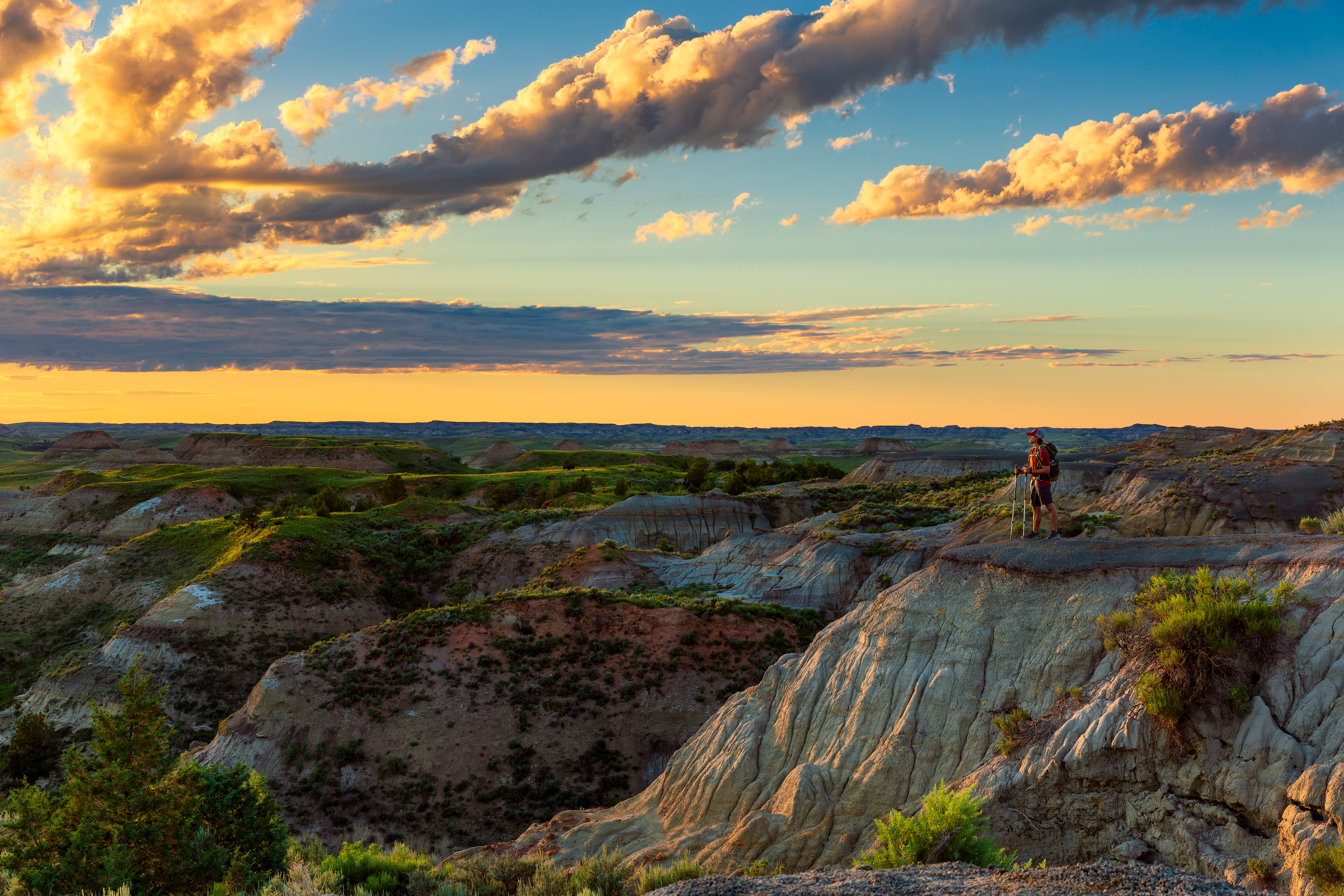 A hiker stands on the edge of a butte looking over the North Dakota badlands.