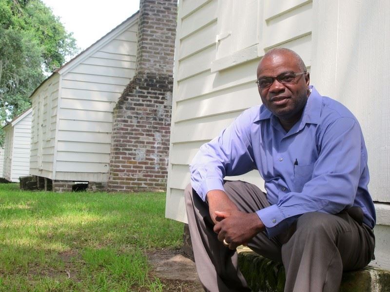 Joe McGill sits in a blue shirt on the steps of white slave cabins