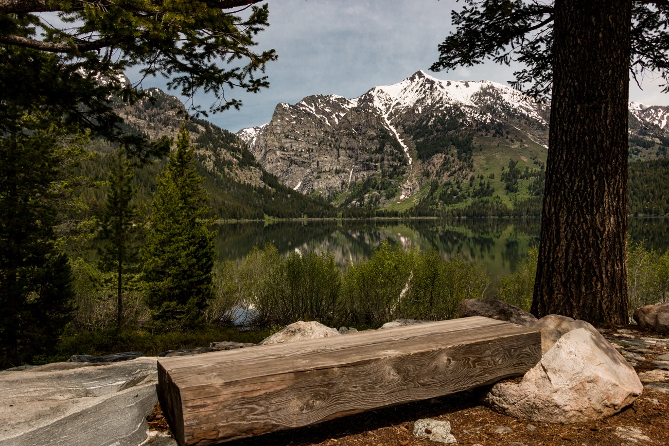 LSR Preserve Trailhead A wooden bench sits beside a lake surrounded by mountains.