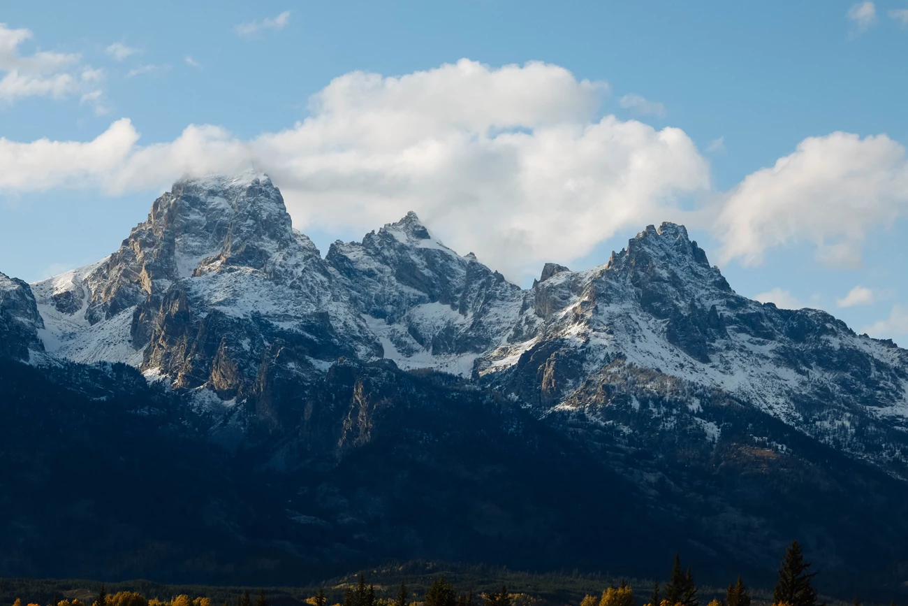 The Teton Range Mountains rise against a partly cloudy sky.