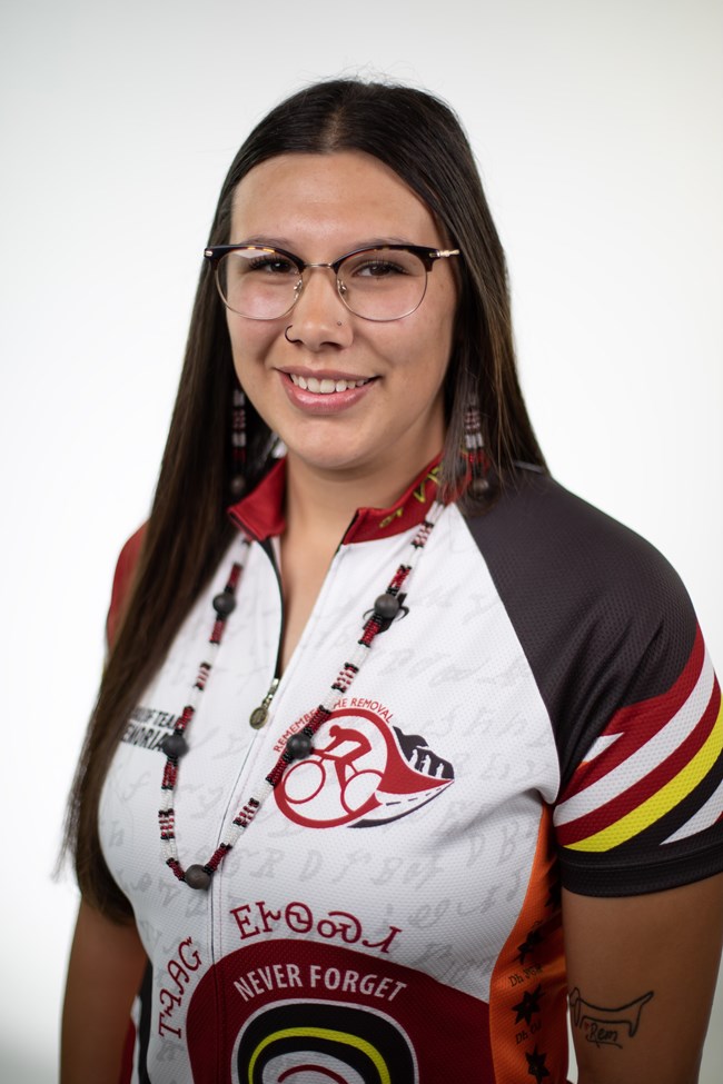 A portrait image of a woman in a cyclist jersey, with dark brown, long hair.