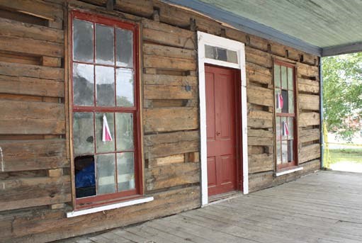 The front of an old wooden cabin with a red door and two large windows.