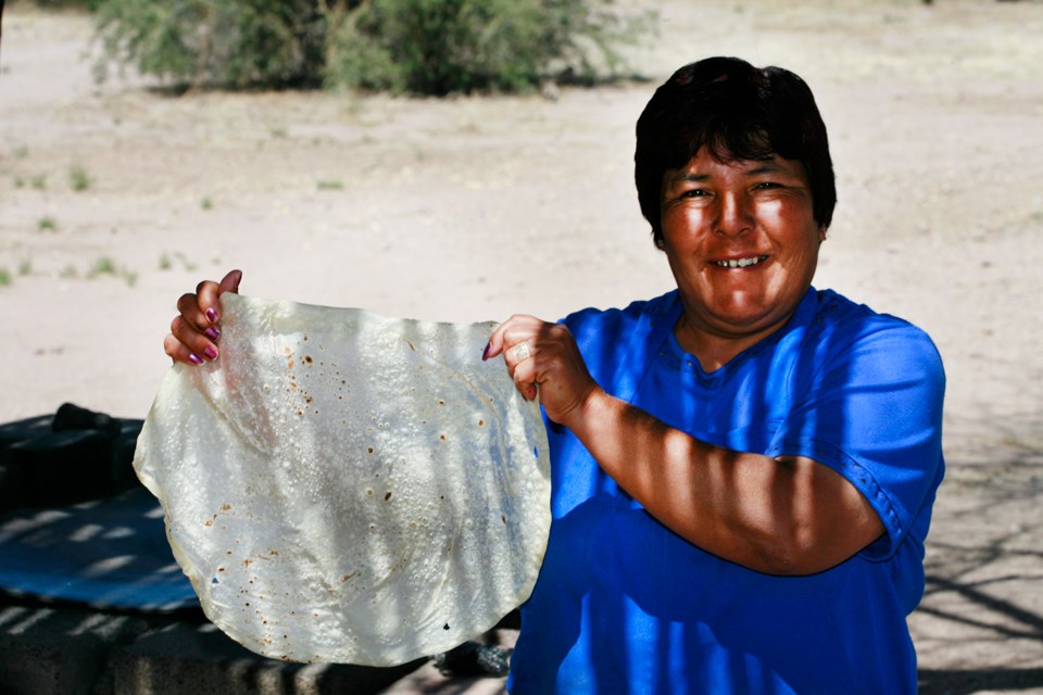 woman holds up a large, finished flour tortilla