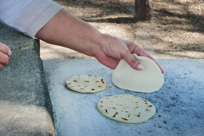 Corn tortillas-on the comal Corn tortilla being place on a hot comal with two others ready to be taken off.
