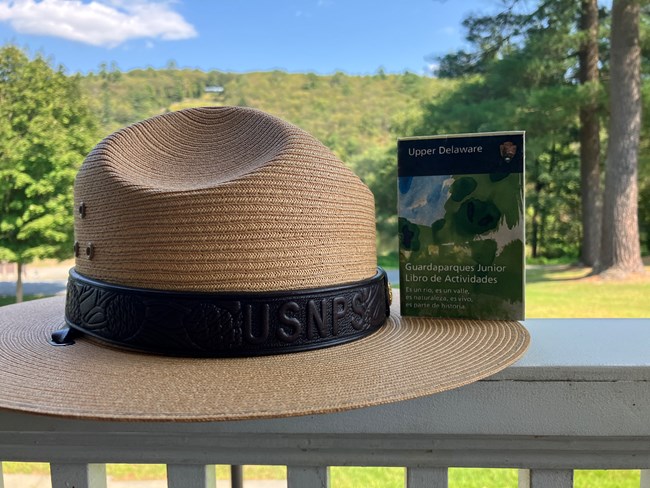 Park ranger straw hat with Upper Delaware Junior Ranger booklet leaning against it. Junior Ranger book text is in Spanish.