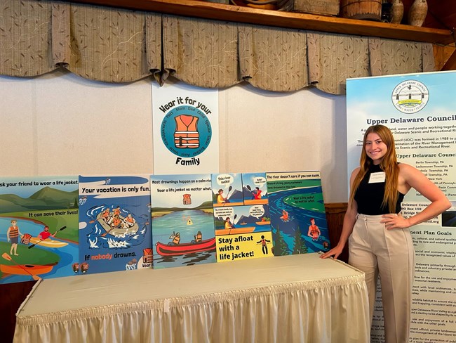 young woman stands next to table with waters and boards containing water safety and life jacket messaging